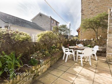 An outdoor patio with a round table and four white chairs surrounded by stone walls and plants at Blueberry Cottage in Sutton Poyntz