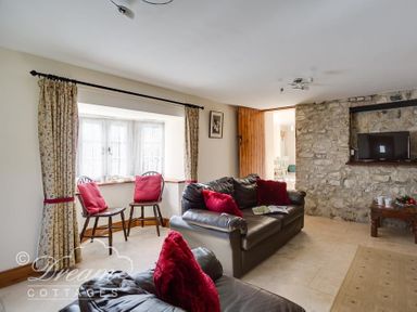 A living room with stone wall a TV two leather sofas with red cushions wooden chairs by a window at Blueberry Cottage in Sutton Poyntz
