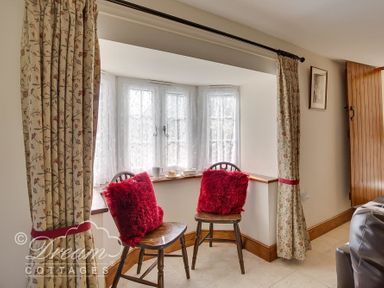A small seating area with two wooden chairs with red pillows near a window with curtains at Blueberry Cottage in Sutton Poyntz