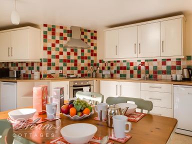 A kitchen with a wooden table set for breakfast and colorful tiled backsplash at Blueberry Cottage in Sutton Poyntz