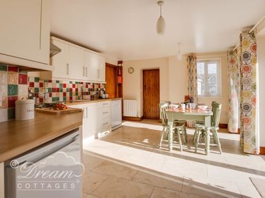 A kitchen with a dining table and chairs next to windows with patterned curtains at Blueberry Cottage in Sutton Poyntz