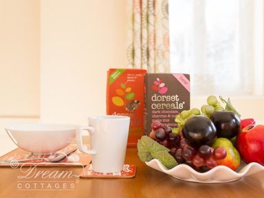 A bowl, a mug, two boxes of Dorset Cereals and a plate of fruit on a wooden table at Blueberry Cottage in Sutton Poyntz