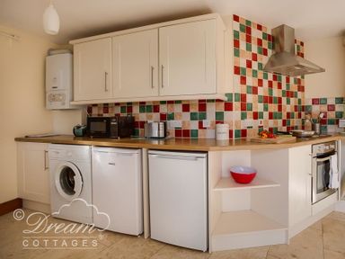 A kitchen with washing machine fridge oven microwave and colorful tiled backsplash at Blueberry Cottage in Sutton Poyntz