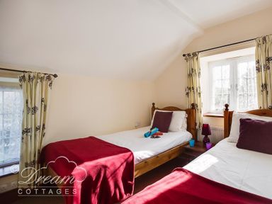 A bedroom with two single wooden beds with red throws and purple cushions at Blueberry Cottage in Sutton Poyntz