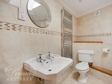 A bathroom with a white sink and toilet and a round mirror above the sink at Blueberry Cottage in Sutton Poyntz