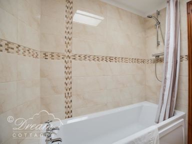 A bathroom with a bathtub shower and tiled walls at Blueberry Cottage in Sutton Poyntz