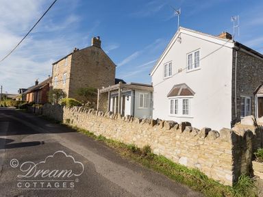 A street view of stone cottages with a stone wall along the road at Blueberry Cottage in Sutton Poyntz