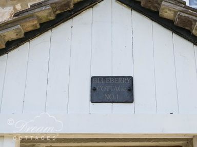 A sign reading Blueberry Cottage No 1 on a white wooden gable at Blueberry Cottage in Sutton Poyntz