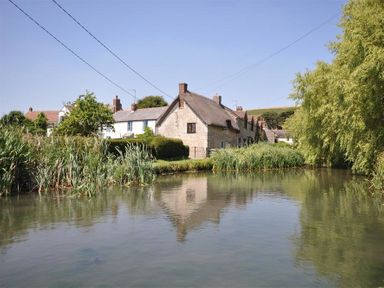 Stone cottages and white houses by a pond with reeds and trees at Blueberry Cottage in Sutton Poyntz