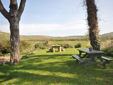 A garden area with two picnic tables and trees overlooking fields at Blueberry Cottage in Sutton Poyntz
