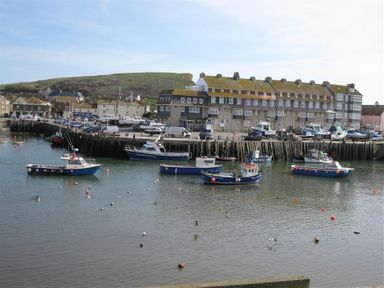 A harbor with boats on the water and buildings along the shore with a hill in the background at The Boardwalk in West Bay