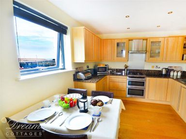 A kitchen with wooden cabinets a dining table set with plates cutlery and a fruit bowl at The Boardwalk in West Bay