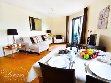 A dining table set with plates cups and fruit bowls next to a living area with sofas lamps and a mirror at The Boardwalk in West Bay