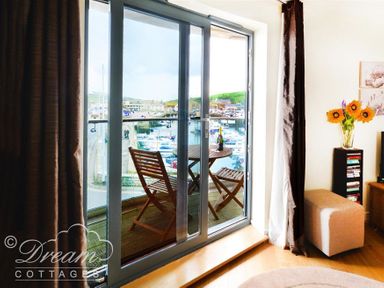 A room with sliding glass doors opening to a balcony with a wooden table and two chairs overlooking a marina at The Boardwalk in West Bay