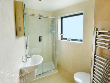 A bathroom with a shower enclosure a sink a toilet a window and a heated towel rail at The Boardwalk in West Bay