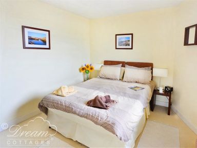 A bedroom with a double bed bedside tables lamps framed photos on walls and a vase with sunflowers at The Boardwalk in West Bay