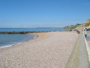A beach with pebbles and a stone seawall with cliffs in the background at The Boardwalk in West Bay
