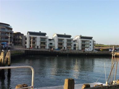 Waterfront view with modern apartment buildings and a harbor with boats at The Boardwalk in West Bay