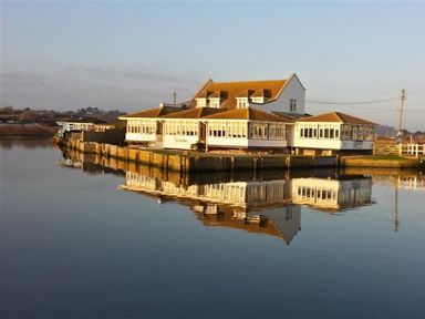 A large white building with many windows beside a calm body of water reflecting the building at The Boardwalk in West Bay