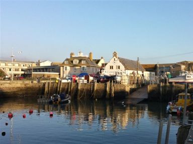 A harbor with boats docked near buildings and a stone pier at The Boardwalk in West Bay