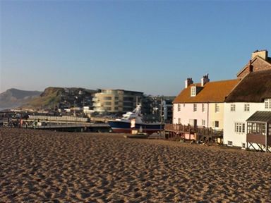 A sandy beach with buildings and a boat near a pier at The Boardwalk in West Bay