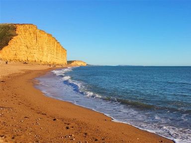A beach with sand and waves and a large cliff in the background at The Boardwalk in West Bay