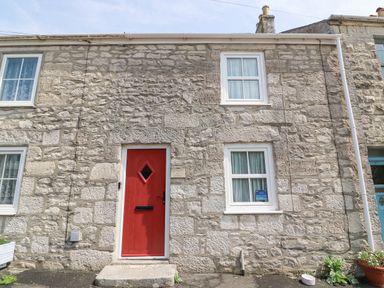 A stone house exterior with a red door and white framed windows at Bowmans Cottage in Wakeham Portland
