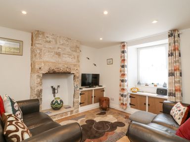 A living room with leather sofas stone fireplace curtains and a TV at Bowmans Cottage in Wakeham Portland