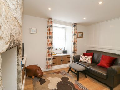 A sitting room with a black leather sofa red cushions a patterned rug and a window with patterned curtains at Bowman's Cottage in Wakeham Portland