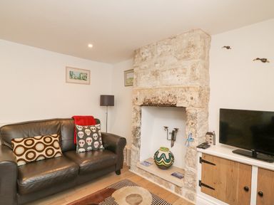 A living room with a black leather sofa and a stone fireplace at Bowman's Cottage in Wakeham Portland