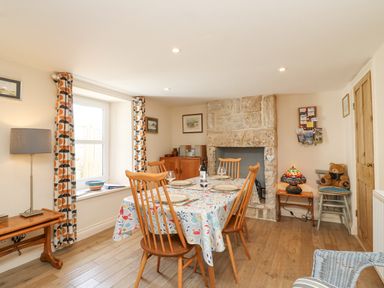 A dining room with a wooden table and chairs a stone fireplace and patterned curtains at Bowmans Cottage Wakeham Portland