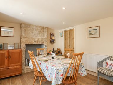 A dining room with a wooden table and chairs a stone fireplace and a wooden cabinet at Bowmans Cottage in Wakeham Portland