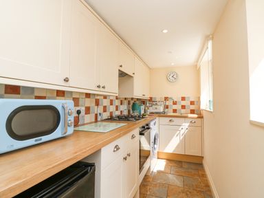 A kitchen with wooden countertops white cabinets a gas stove a blue microwave a washing machine and a clock on the wall at Bowmans Cottage in Wakeham Portland
