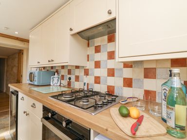 A kitchen countertop with a gas stove microwave and cutting board with fruit and bottles at Bowmans Cottage in Wakeham Portland