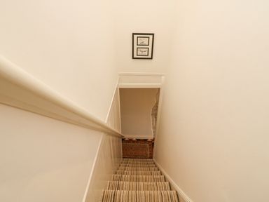 A staircase with striped carpet and a handrail on the left with framed artwork on the wall at Bowmans Cottage in Wakeham Portland