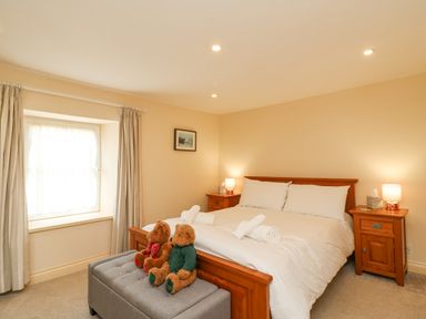 A bedroom with a double bed bedside tables with lamps a window with curtains and two teddy bears sitting on a bench at Bowman's Cottage in Wakeham Portland