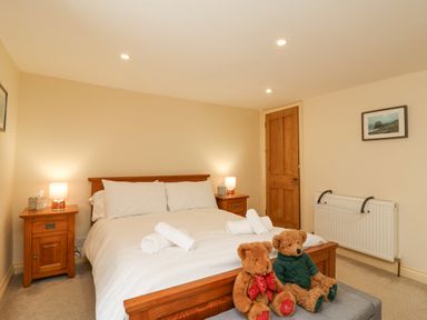 A bedroom with a wooden bed with white bedding two bedside tables with lamps two teddy bears on a bench at Bowman's Cottage in Wakeham Portland