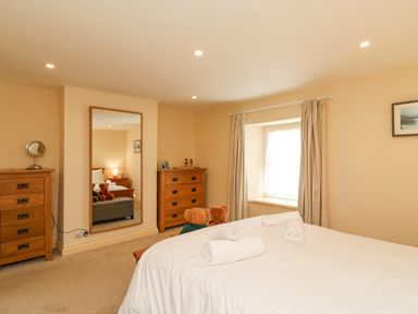 A bedroom with a bed towels on it two wooden dressers a large mirror window with curtains and two teddy bears at Bowmans Cottage in Wakeham Portland
