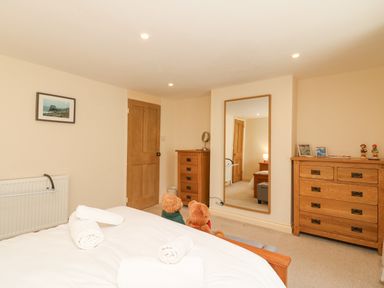 A bedroom with a bed and rolled towels two wooden dressers a large mirror and teddy bears at Bowmans Cottage in Wakeham Portland