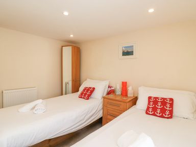 A bedroom with two single beds with white bedding and red anchor pillows at Bowman's Cottage in Wakeham Portland