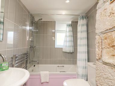A bathroom with a bathtub shower combination a striped shower curtain a white sink a toilet and tiled walls at Bowmans Cottage in Wakeham Portland