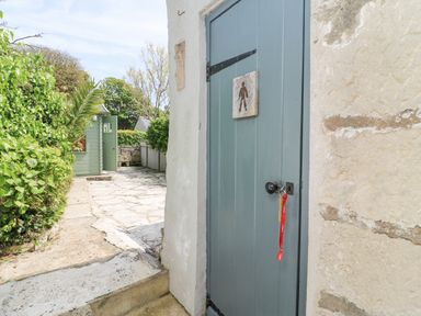A blue wooden door with a key in the lock and a sign on it next to a stone path and green bushes at Bowman's Cottage in Wakeham Portland