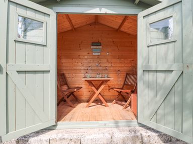 A small wooden shed with open double doors revealing two wooden chairs and a wooden table inside Bowmans Cottage Wakeham Portland