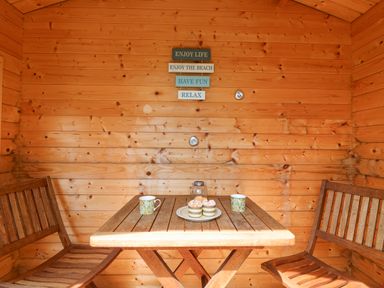 A wooden seating area with a table two chairs mugs and cupcakes on a plate at Bowman's Cottage in Wakeham Portland