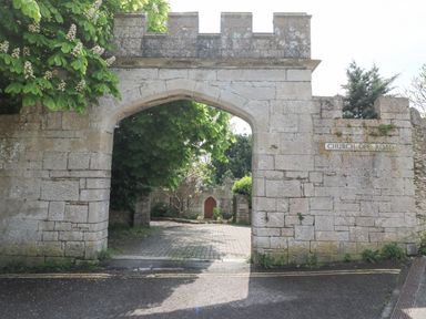 A stone archway entrance with a sign reading Church Ope Road and trees inside at Bowman's Cottage in Wakeham Portland