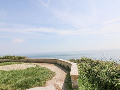 A coastal viewpoint with a low stone wall and grassy area overlooking the sea at Bowman's Cottage in Wakeham Portland