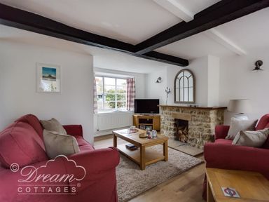 A living room with red sofas a wooden coffee table and a stone fireplace at Bramble Cottage in Burton Bradstock