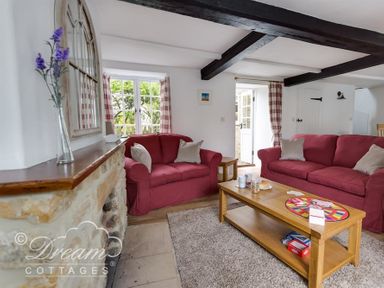 A living room with red sofas wooden coffee table and stone fireplace at Bramble Cottage in Burton Bradstock