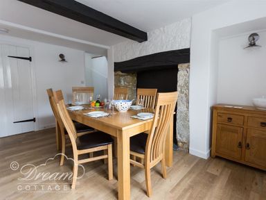 A dining room with a wooden table and six chairs near a stone fireplace and a wooden cabinet at Bramble Cottage in Burton Bradstock