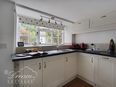 A kitchen with cream cabinets black countertops a window with polka dot blinds and red appliances at Bramble Cottage in Burton Bradstock